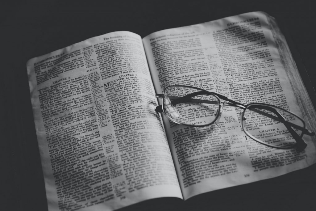 grayscale photo of eyeglasses on top of book